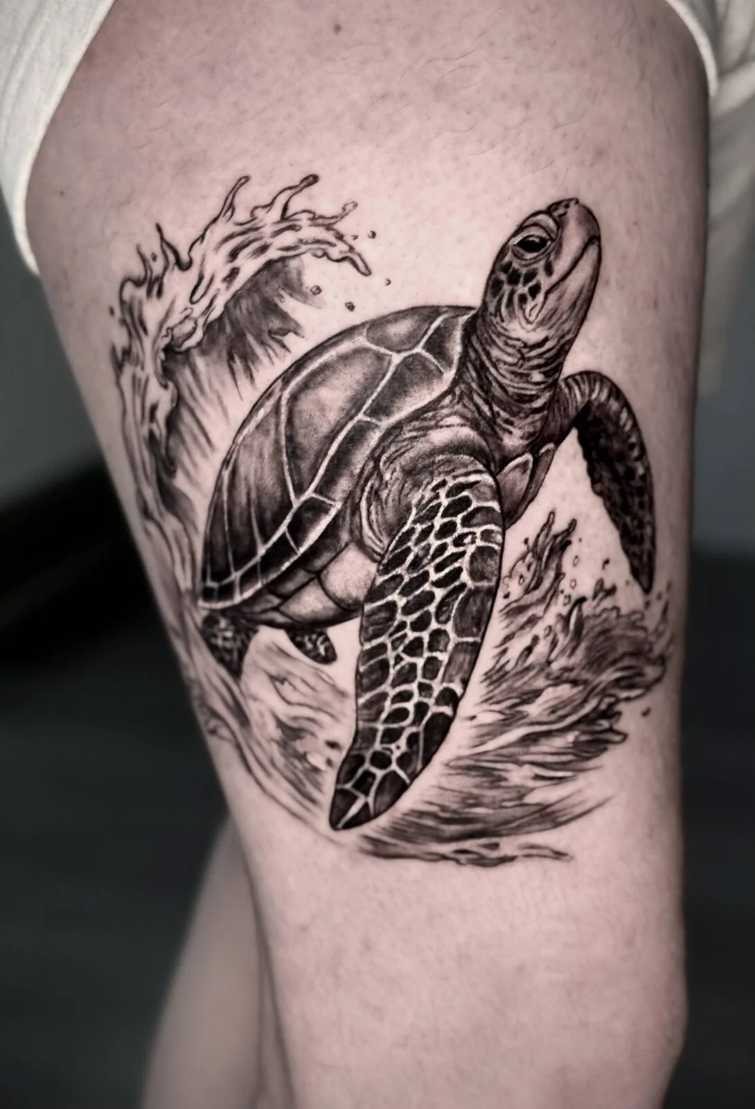 Black and grey sea turtle and wave tattoo on an upper arm