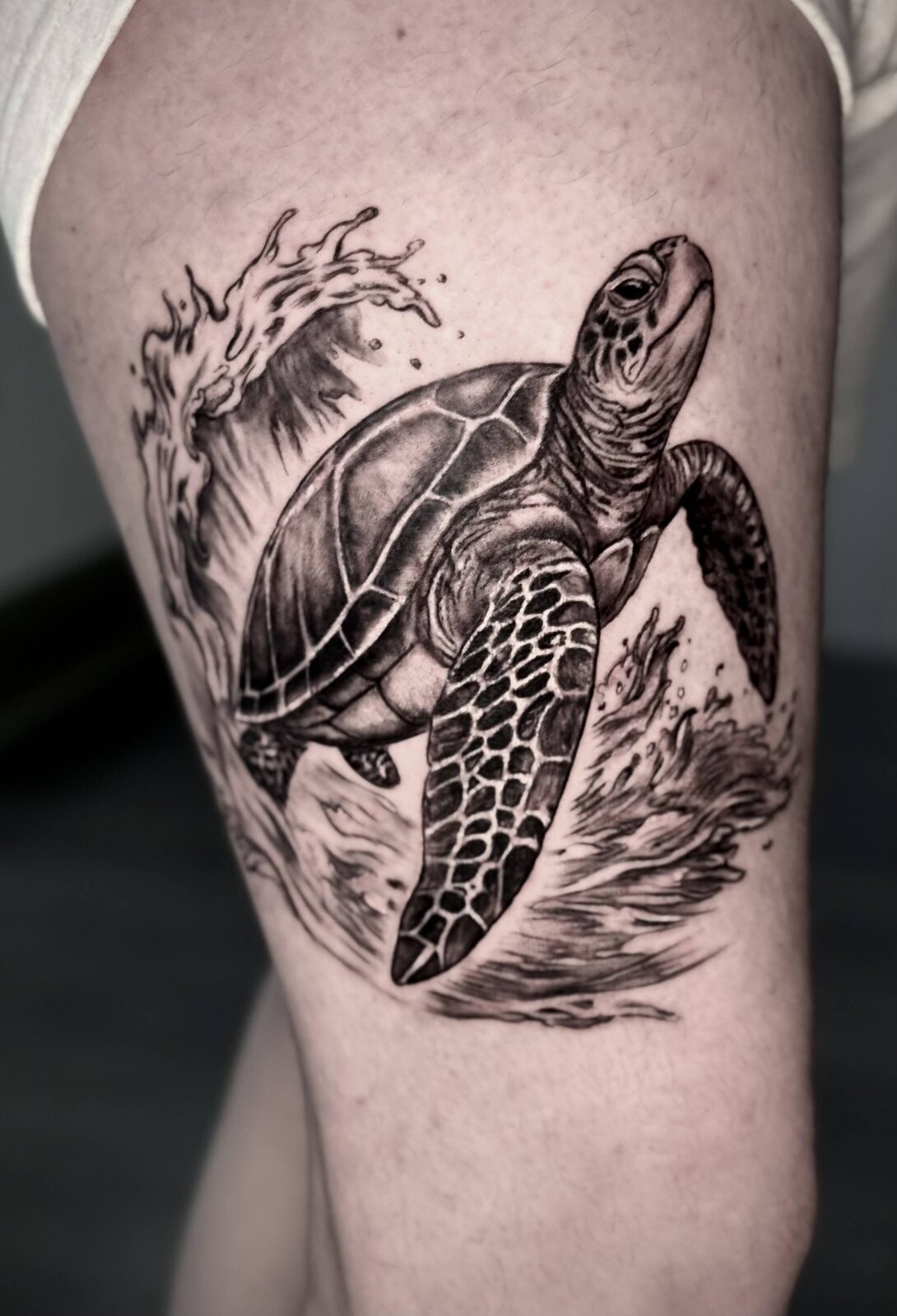 Black and grey sea turtle and wave tattoo on an upper arm