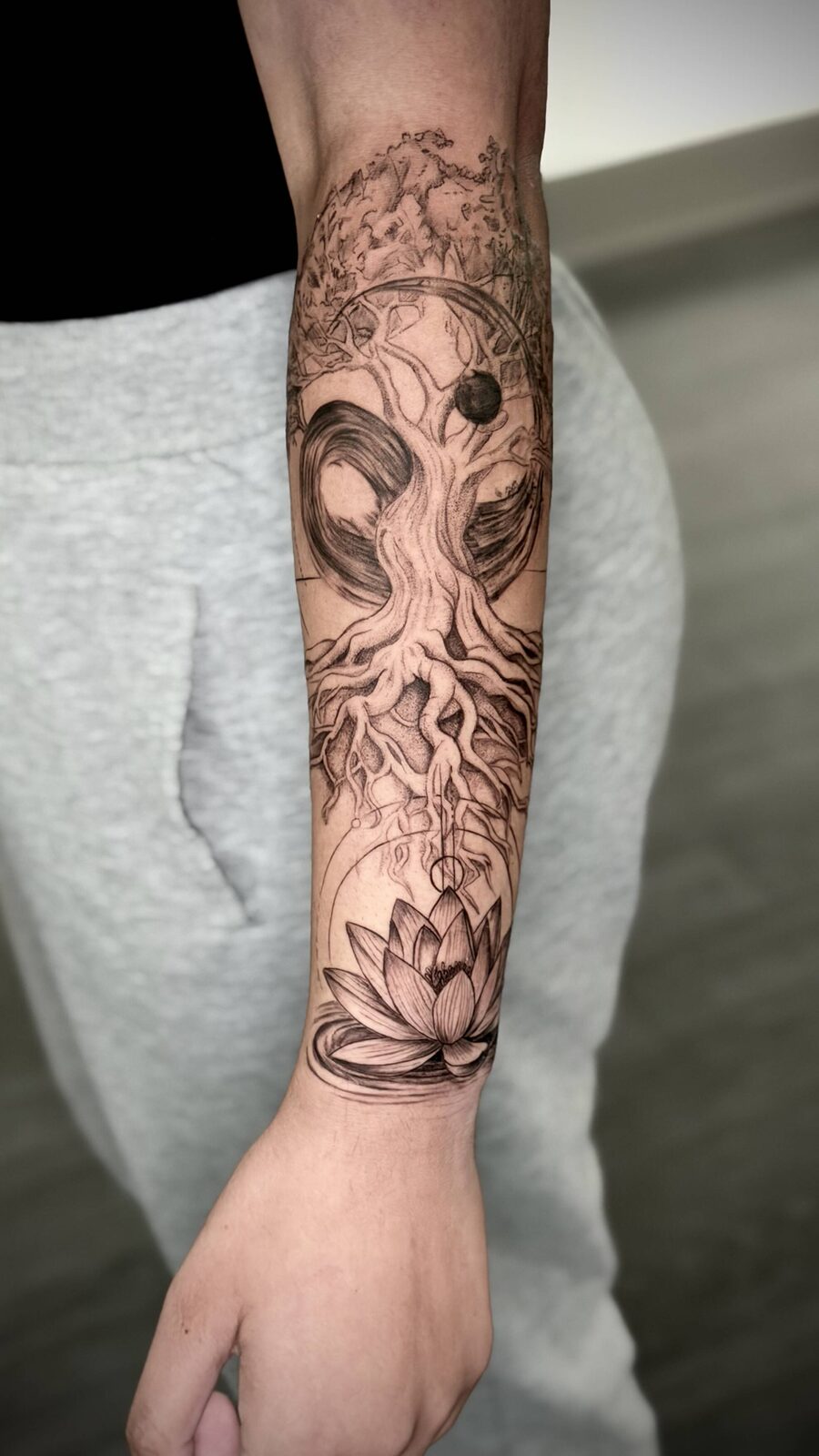 Ornamental black and grey forearm sleeve tattoo with lotus